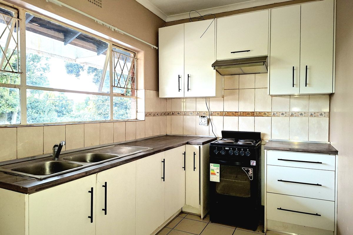 Functional kitchen featuring white cabinetry, laminate countertops, a stainless steel double sink, and a freestanding stove with an extractor fan.