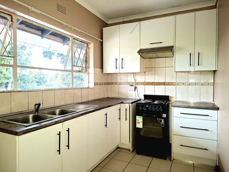 Functional kitchen featuring white cabinetry, laminate countertops, a stainless steel double sink, and a freestanding stove with an extractor fan.
