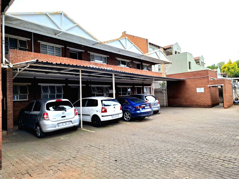 Exterior view of a brick apartment building featuring a covered carport area and paved driveway parking.