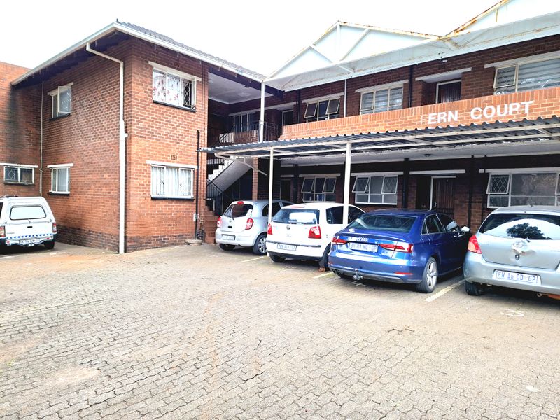 Front exterior view of Fern Court apartment complex featuring brick facade, covered parking bays, and paved driveway area.