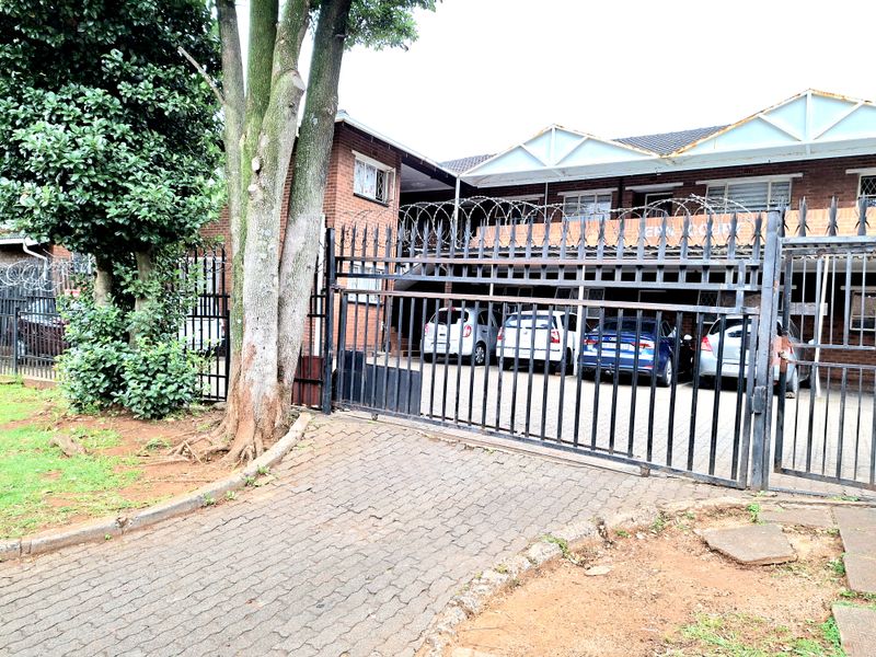 Front exterior view of an apartment complex featuring a brick facade, paved driveway, and secure gated entrance with perimeter razor wire.