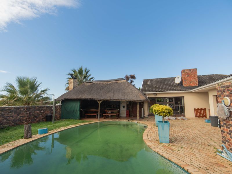 Outdoor entertainment area featuring a swimming pool, brick paved patio, and a traditional thatch roof lapa, set within a private garden space.