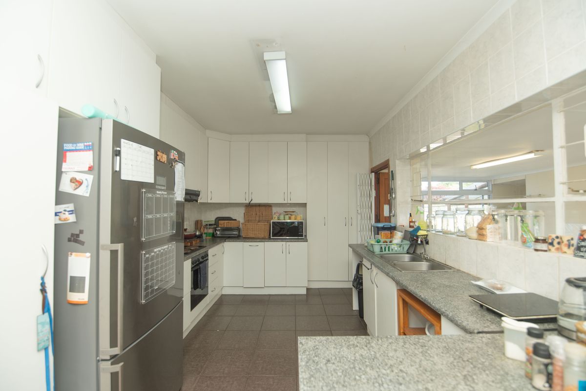 A functional kitchen featuring white cabinetry, granite countertops, a double basin sink, and tiled flooring with a convenient serving window to the adjacent room.