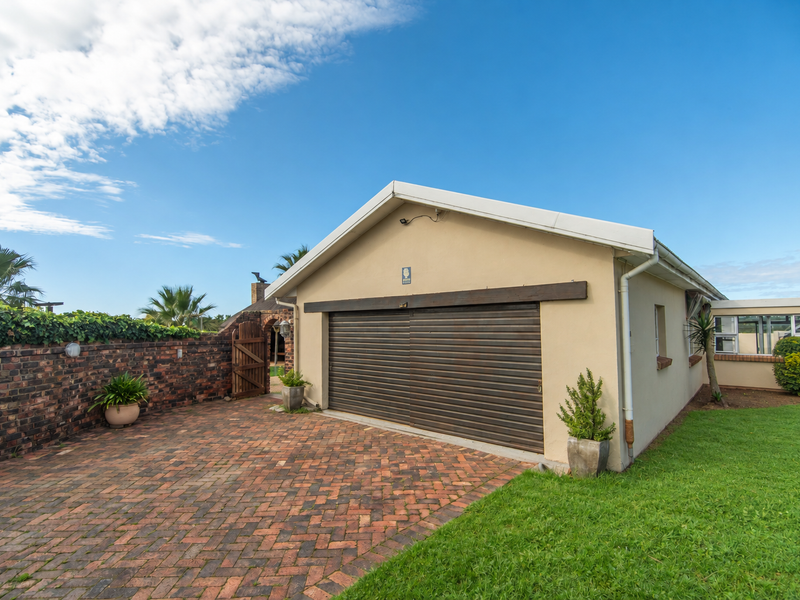 Exterior view of a detached garage featuring a roller shutter door, brick paved driveway, and surrounding brick boundary wall.
