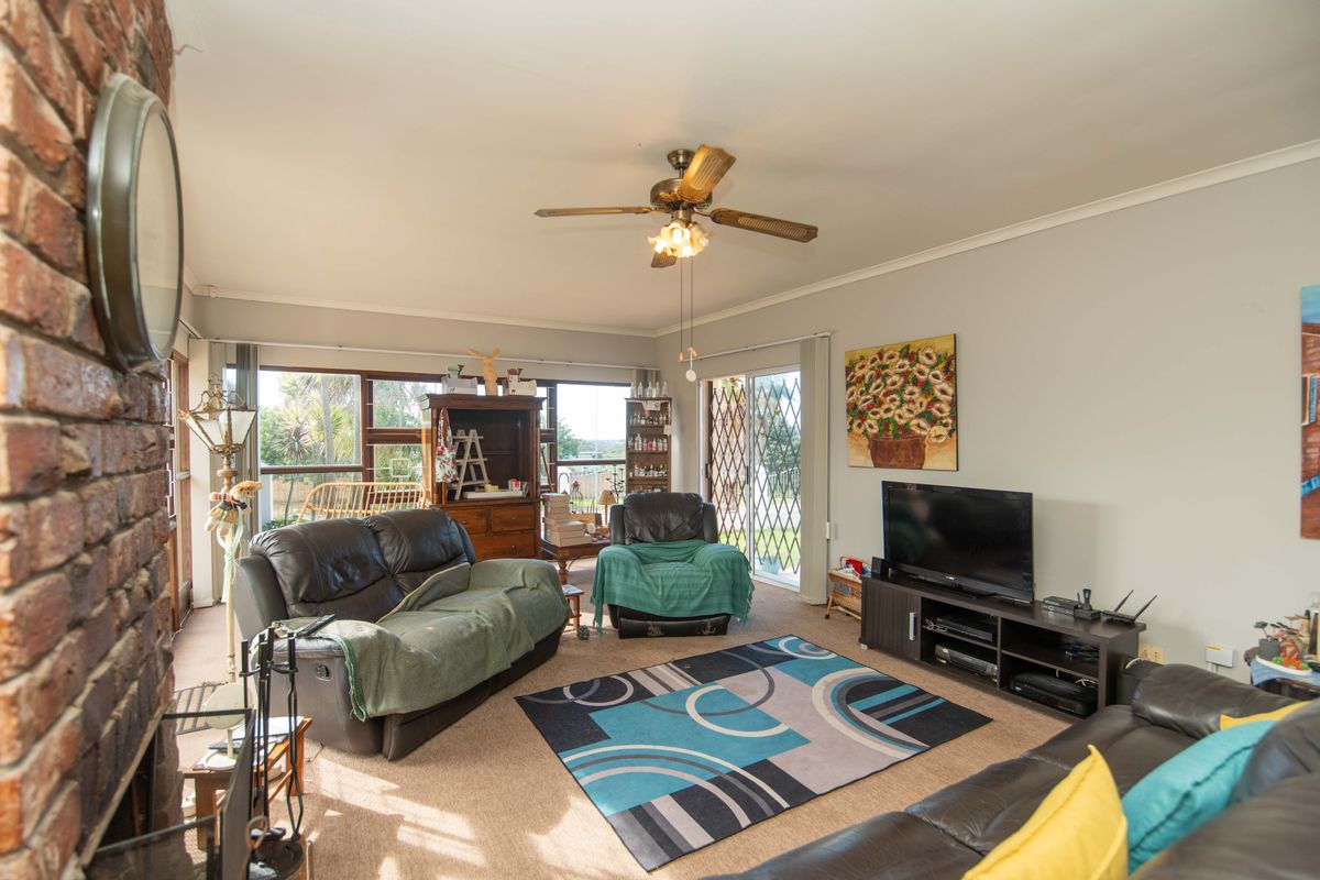 Spacious living room featuring a prominent brick fireplace, ceiling fan, and large windows with sliding glass doors providing natural light and outdoor access.