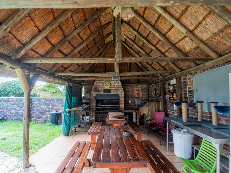 Covered outdoor entertainment area featuring a traditional thatched roof, exposed timber trusses, and a built-in brick braai, perfect for alfresco dining.