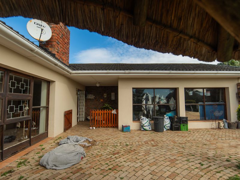 A paved outdoor patio area featuring a brick chimney and thatched roof overhang, providing a functional space for outdoor living.