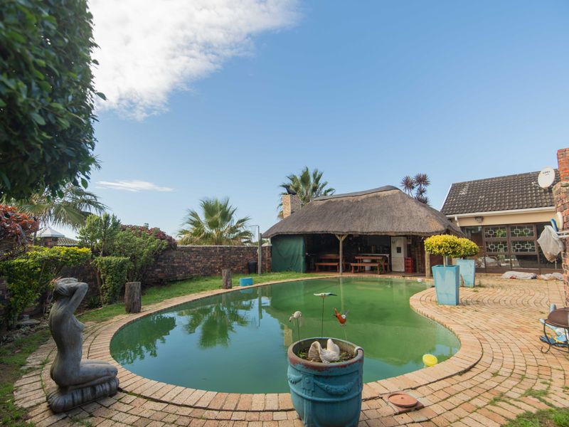 Outdoor pool area featuring a swimming pool, brick paving, and a thatched lapa structure in the rear garden.
