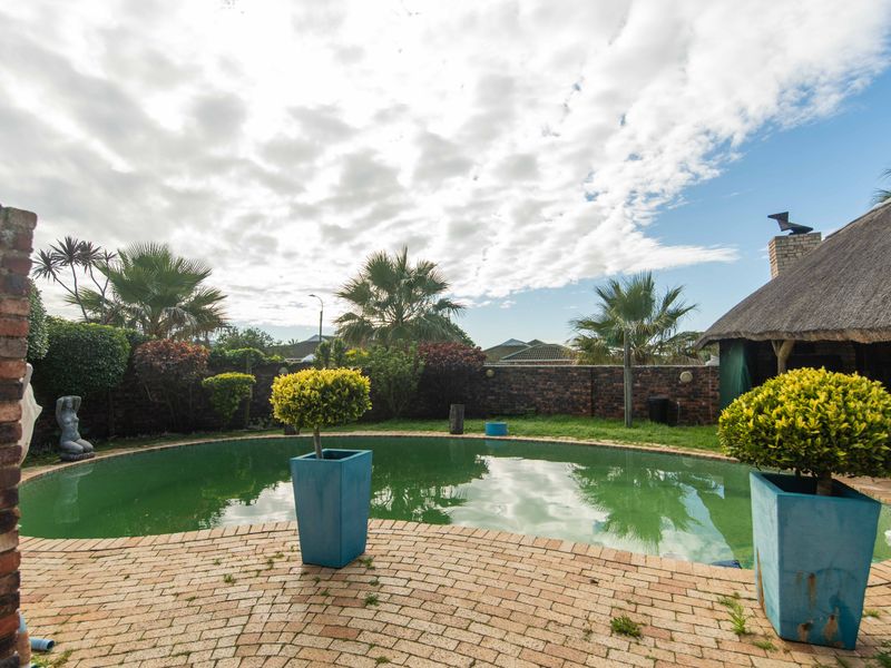 Outdoor pool area featuring a swimming pool, brick paving, and a thatch roof structure, enclosed by a brick boundary wall.