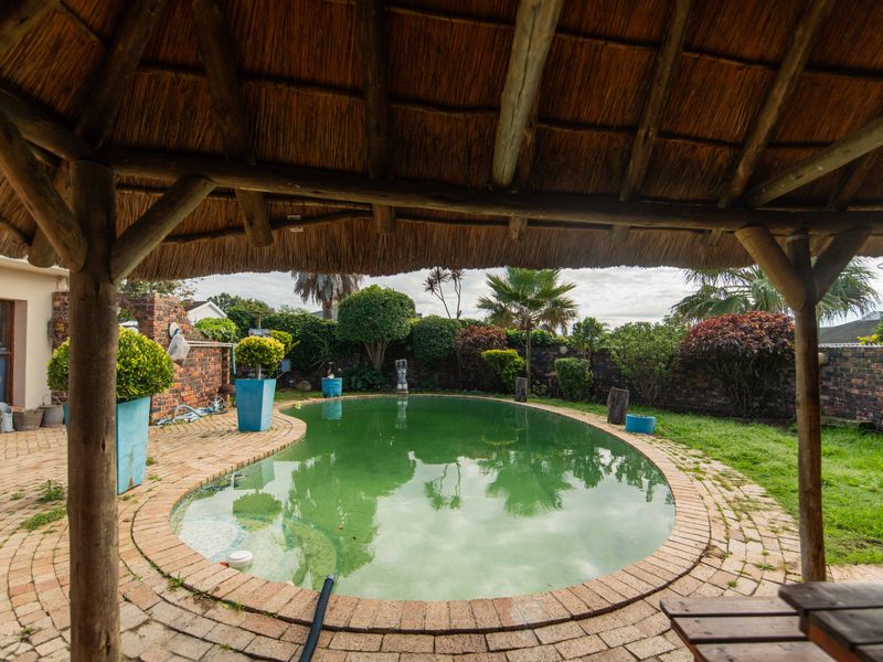 Outdoor pool area featuring a thatched lapa, brick paved surround, and a private garden enclosed by a brick boundary wall.