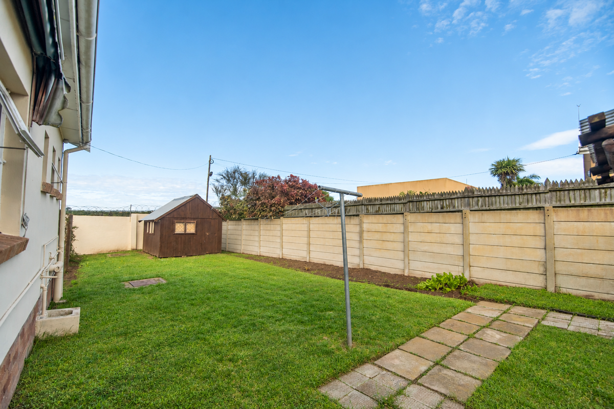 A private rear garden featuring a lawn, paved pathway, wooden storage shed, and secure precast concrete boundary walling.
