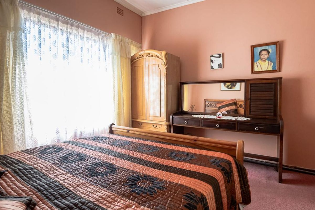 A bedroom featuring pink walls, carpeted flooring, and a large window with natural light.
