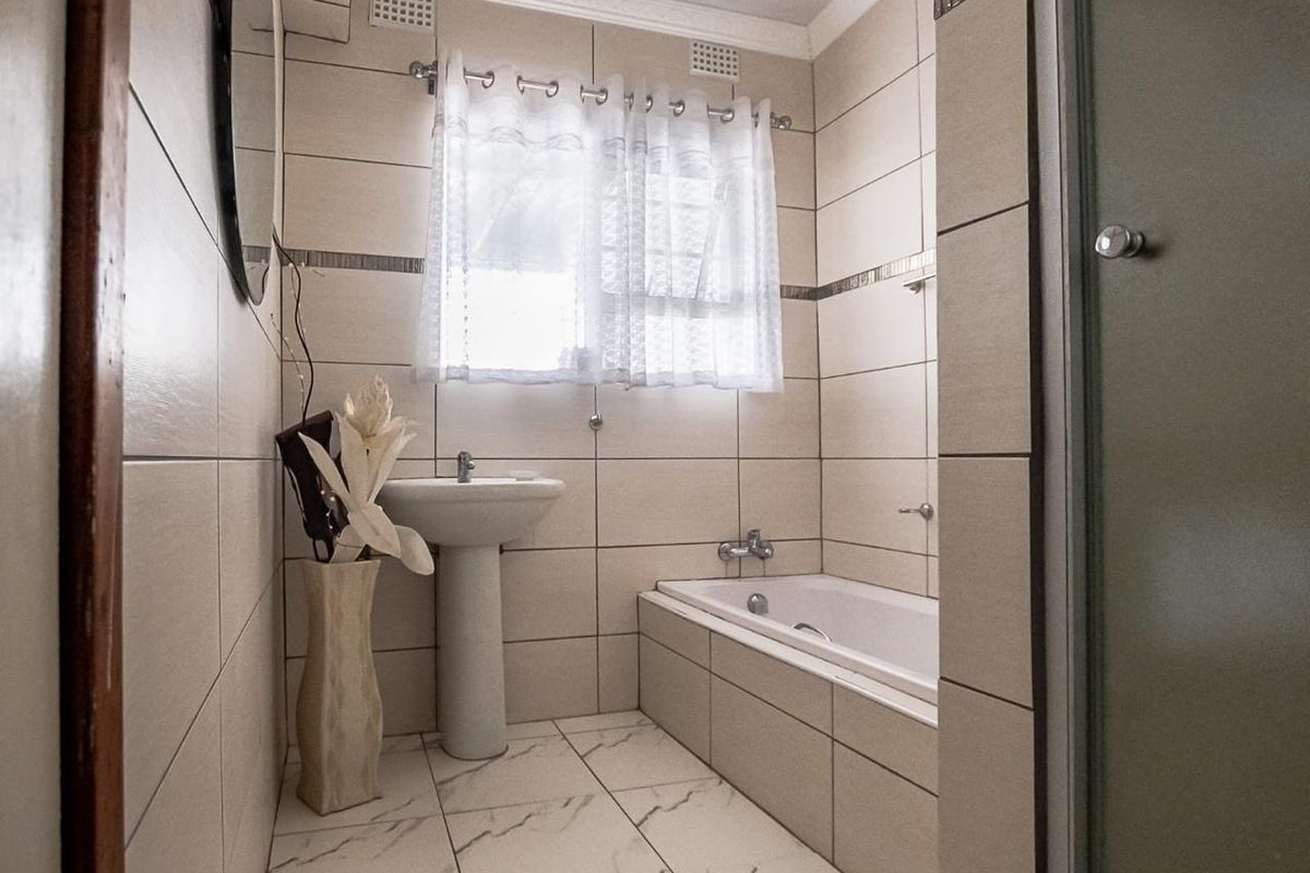 A functional bathroom featuring a pedestal basin, built-in bathtub, and neutral floor-to-ceiling tiling with decorative accents.