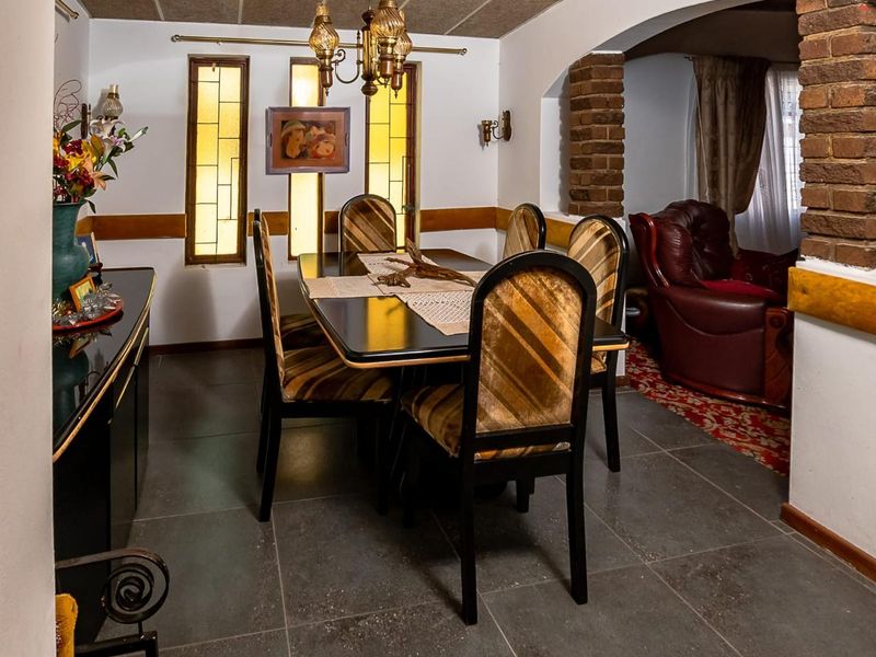 Dining room featuring tiled flooring, exposed brick archway, and stained glass windows, leading into an adjacent living area.