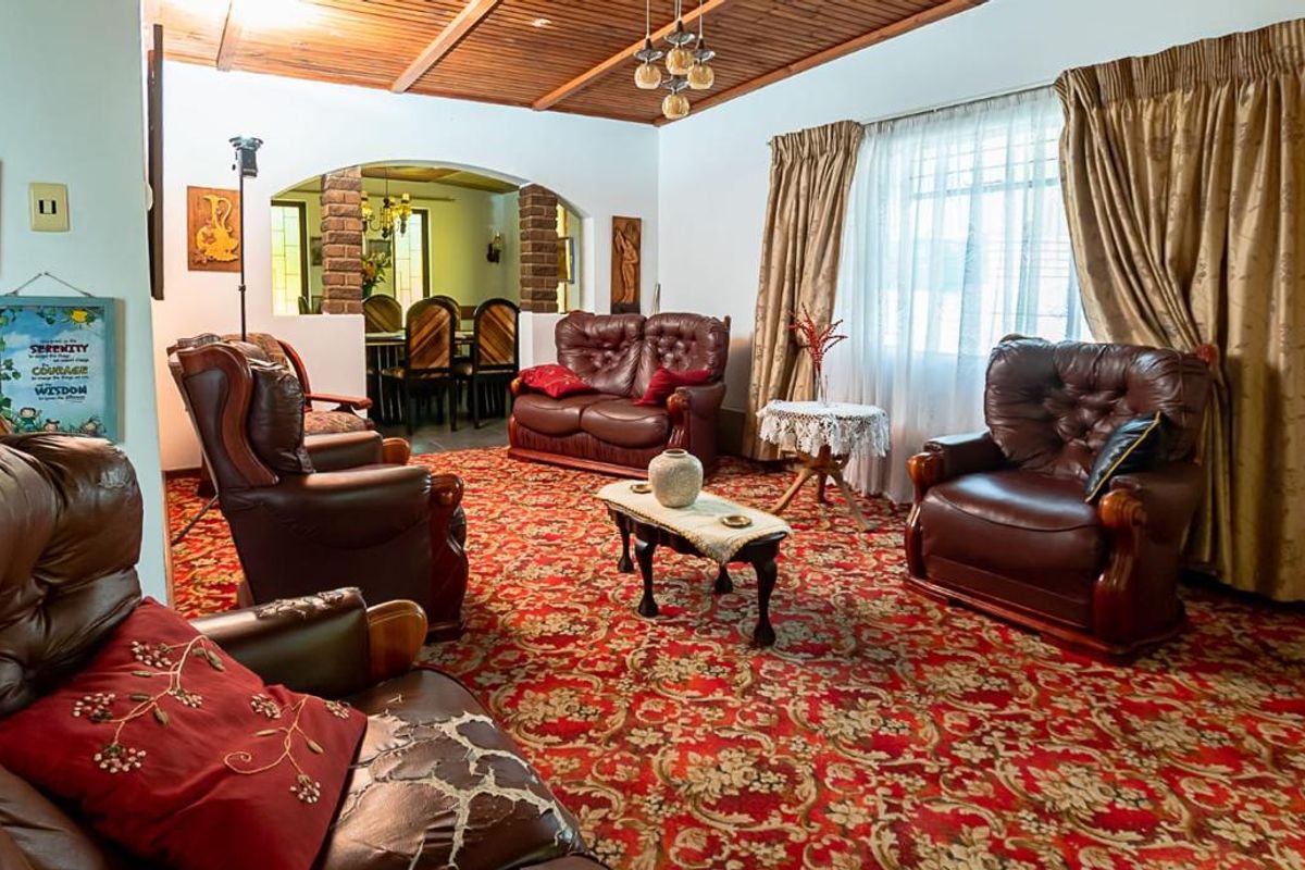 Spacious living room featuring an exposed timber beam ceiling and a brick archway leading to the dining area, with dated carpet flooring.