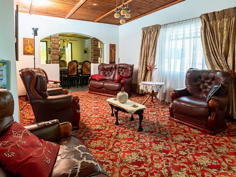 Spacious living room featuring an exposed timber beam ceiling and a brick archway leading to the dining area, with dated carpet flooring.
