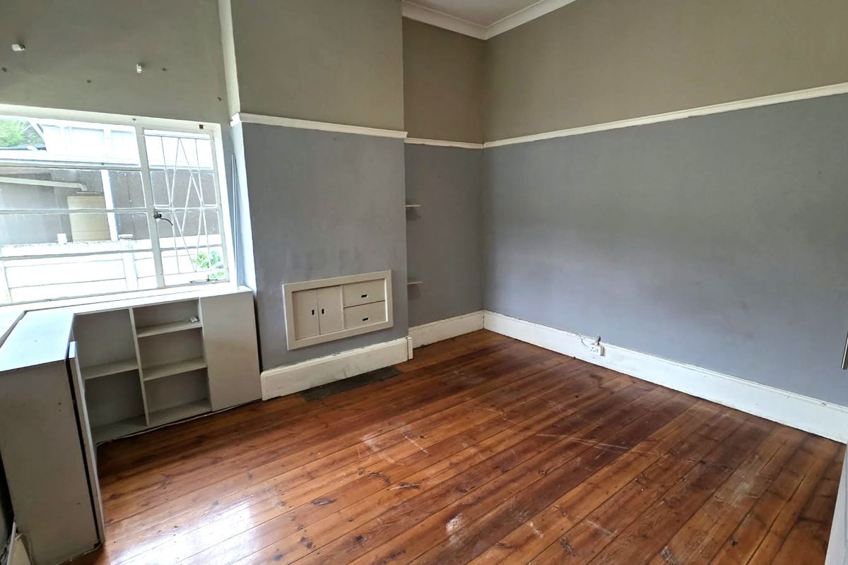An empty bedroom featuring original hardwood flooring, built-in storage cabinetry, and large windows with security bars.