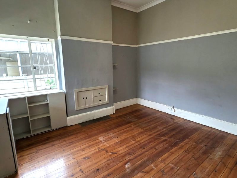 An empty bedroom featuring original hardwood flooring, built-in storage cabinetry, and large windows with security bars.
