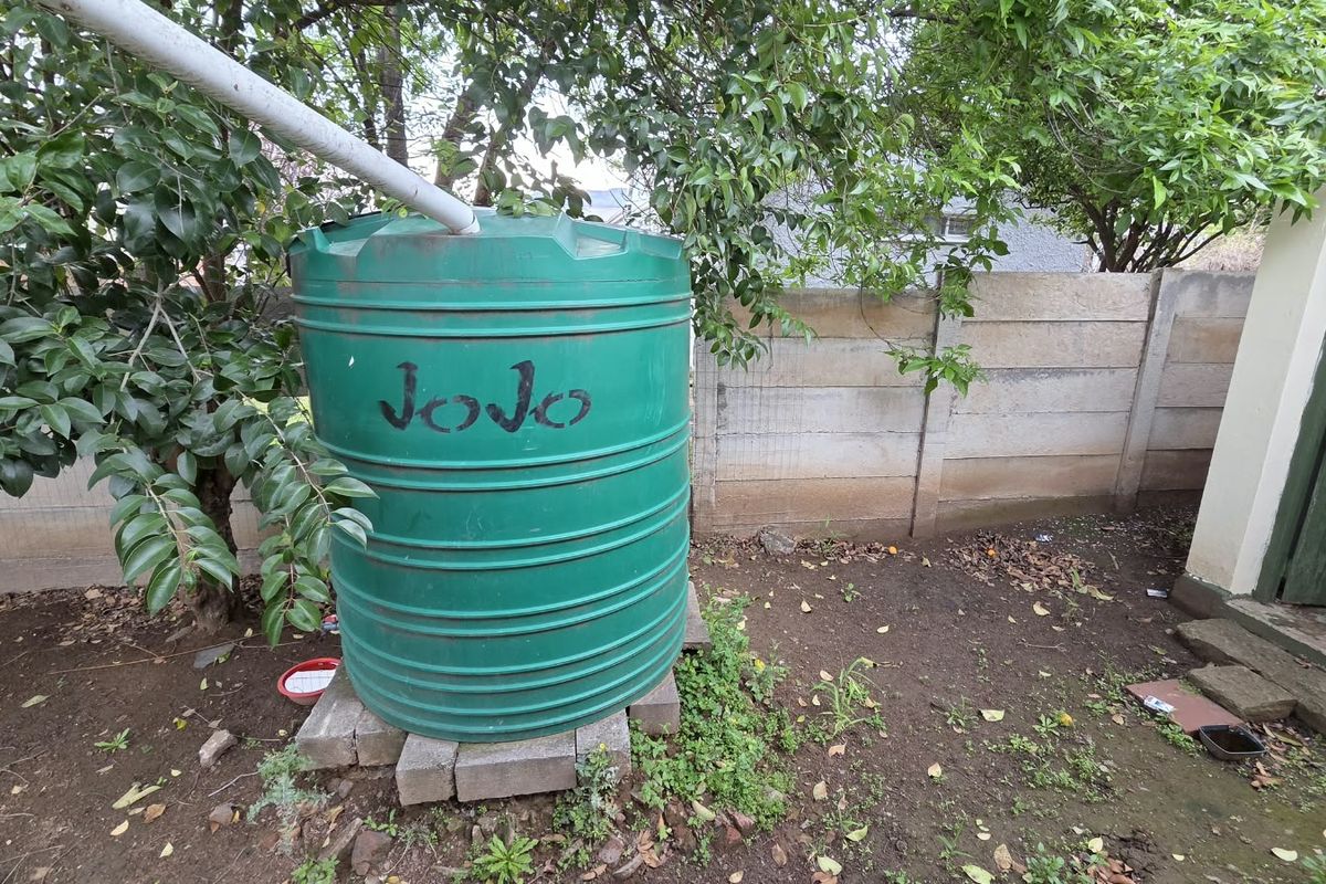 Rear garden area featuring a green water storage tank positioned against a precast concrete boundary wall.