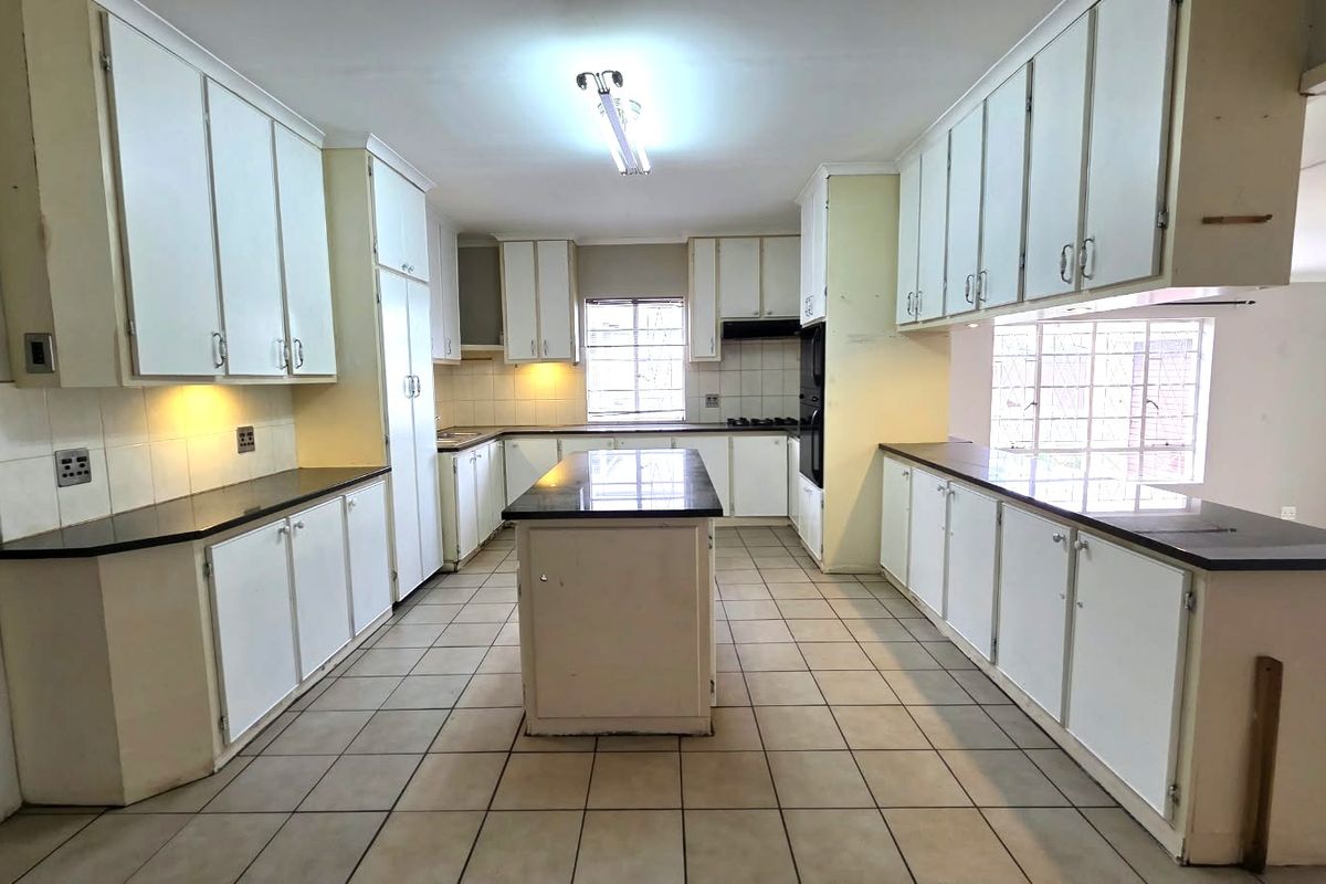 Spacious kitchen featuring extensive built-in cabinetry, a central island with stone countertops, built-in oven, and tiled flooring throughout.