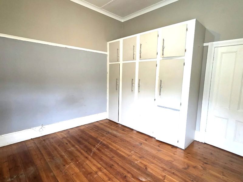 A vacant bedroom featuring original timber flooring, built-in storage cupboards, and classic architectural details including a picture rail and coved ceiling.