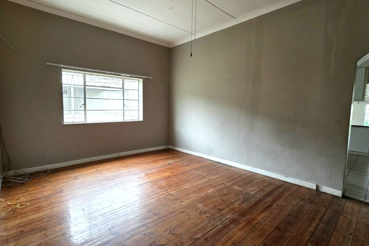An empty living room featuring original hardwood flooring, a steel-framed window with security bars, and an arched entryway leading to an adjacent space.