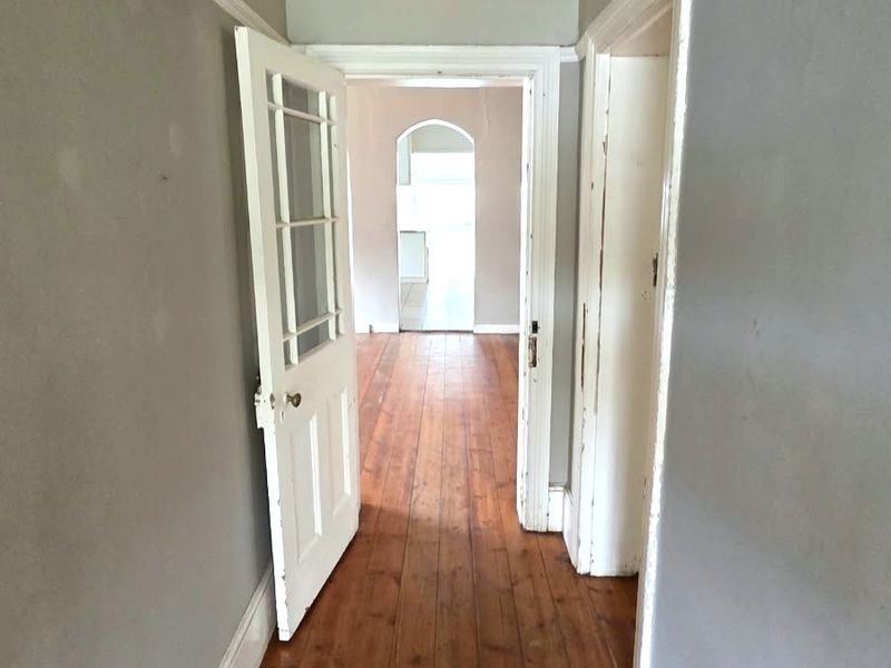 A vacant hallway featuring original timber flooring, classic architrave detailing, and an arched transition leading into the adjoining living space.