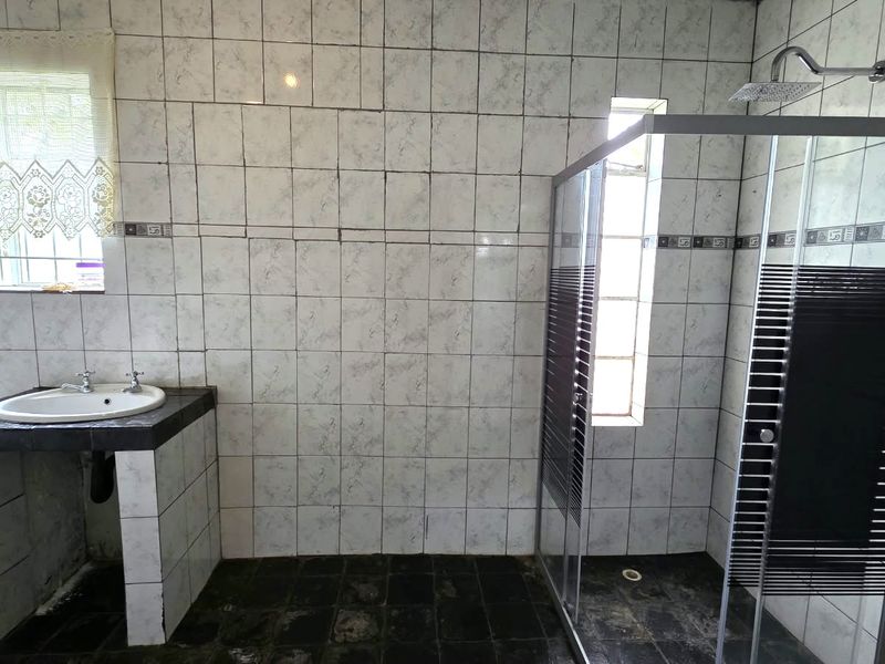 A bathroom featuring a shower enclosure, tiled walls, and a vanity basin. The space requires cosmetic updates to improve its overall condition.