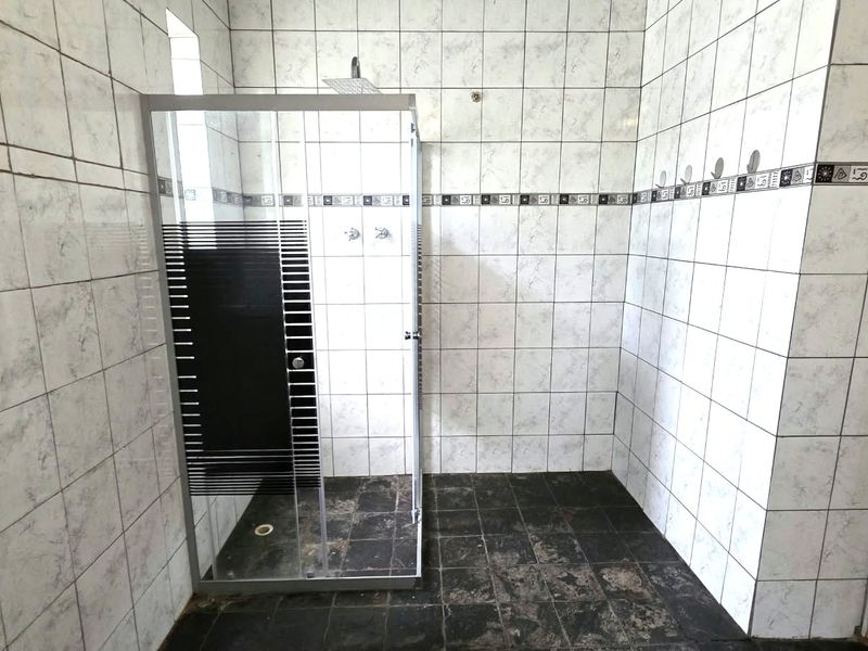 A functional bathroom featuring a glass shower enclosure with tiled walls and dark floor tiling, presenting a dated aesthetic ready for modernization.
