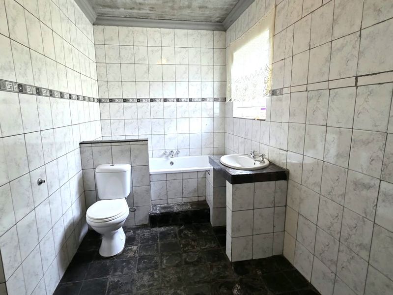 A dated bathroom featuring full-height wall tiling, a built-in bathtub, and a pedestal vanity, offering significant potential for a modern renovation.