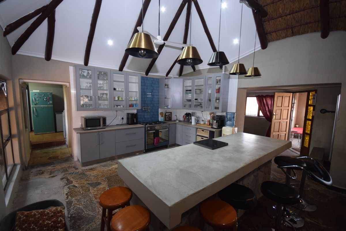 Spacious kitchen featuring a large concrete island, grey cabinetry, gas stove, and unique architectural elements including exposed timber rafters and a thatched ceiling.
