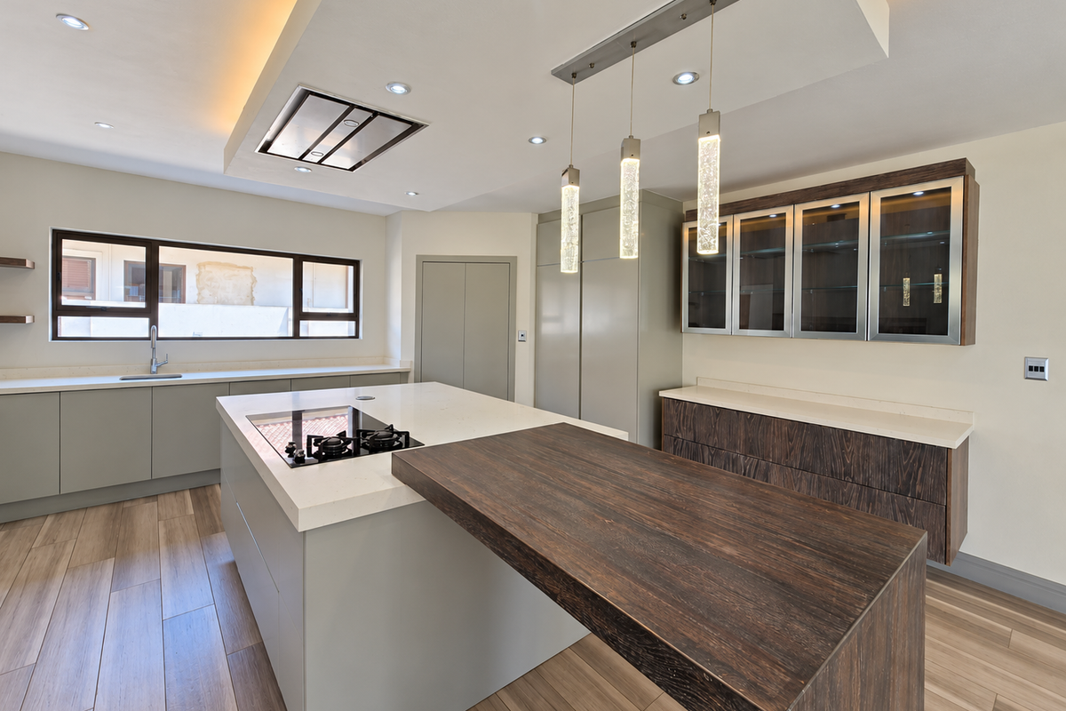 Modern kitchen featuring a large island with integrated hob, stone countertops, custom cabinetry, and stylish pendant lighting in a bright, open-plan layout.