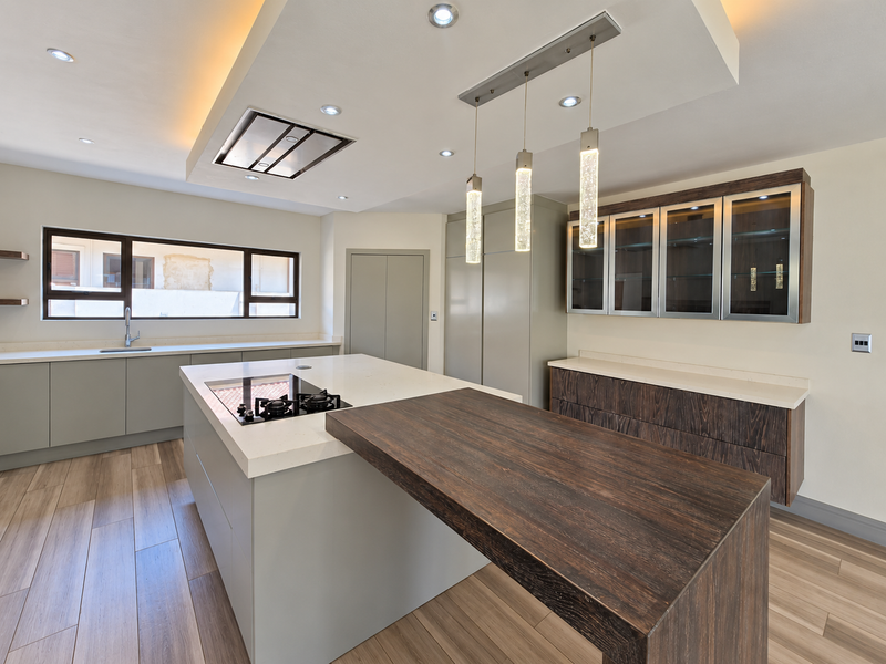Modern kitchen featuring a large island with integrated hob, stone countertops, custom cabinetry, and stylish pendant lighting in a bright, open-plan layout.