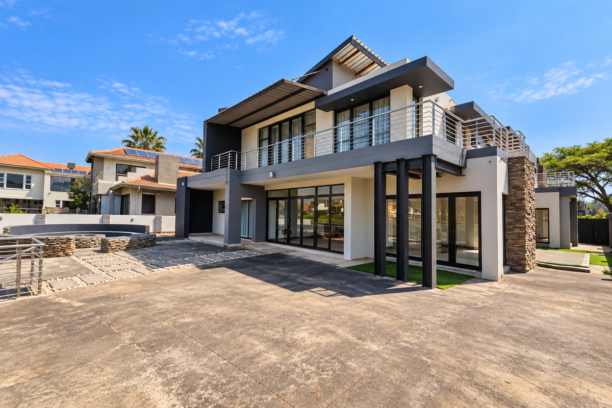 Modern multi-story residence featuring stone cladding, expansive glass sliding doors, a spacious paved patio, and a balcony with metal railings.