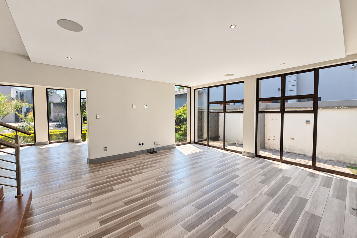 Spacious, light-filled living area featuring modern wood-look tile flooring, recessed ceiling lights, and large windows providing views of the exterior.