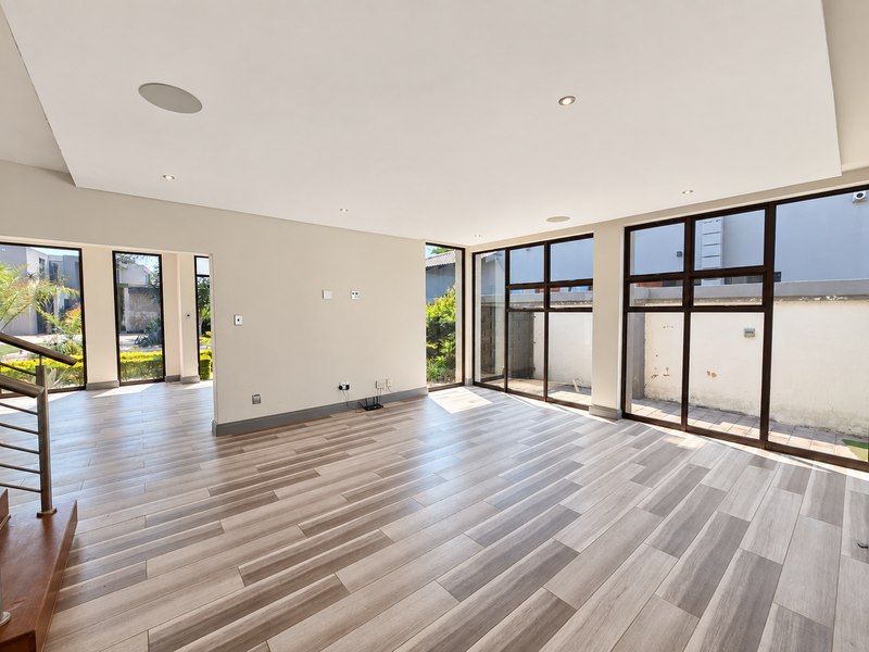 Spacious, light-filled living area featuring modern wood-look tile flooring, recessed ceiling lights, and large windows providing views of the exterior.