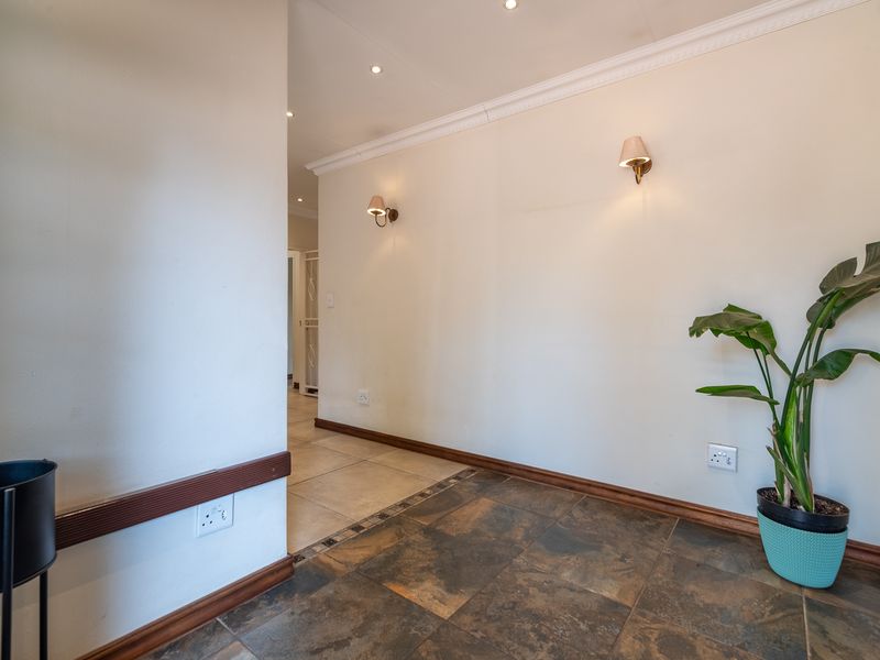 A clean and well-lit hallway featuring tiled flooring, decorative wall sconces, and recessed ceiling lighting, providing a neutral transition space.