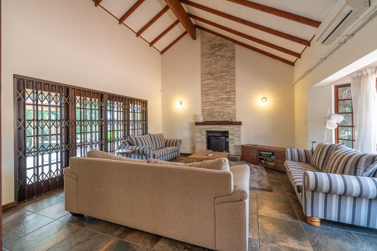 Spacious living room featuring a vaulted ceiling with exposed timber beams, a stone-clad fireplace, and tiled flooring with access to the patio.