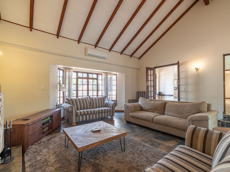Spacious living room featuring a high vaulted ceiling with exposed timber beams, a stone fireplace, tiled flooring, and a large bay window.