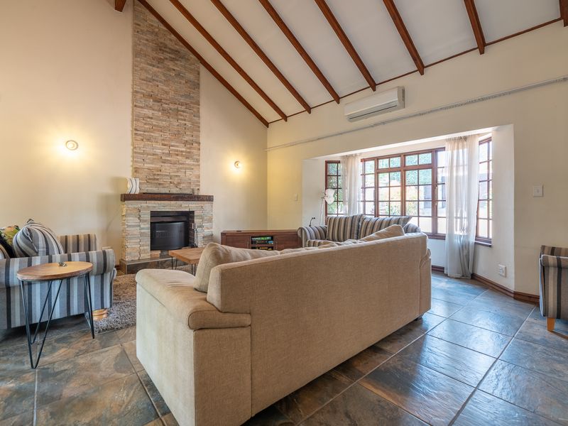 Spacious living room featuring a striking stone-clad fireplace, high vaulted ceilings with exposed timber beams, and large windows allowing for ample natural light.