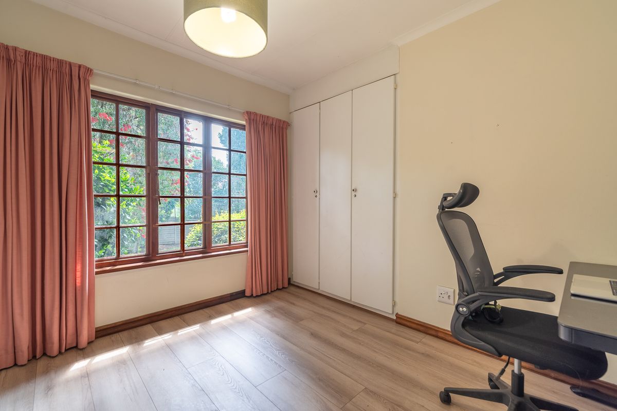 A bedroom featuring laminate flooring, built-in cupboards, and large timber-framed windows providing natural light and garden views.