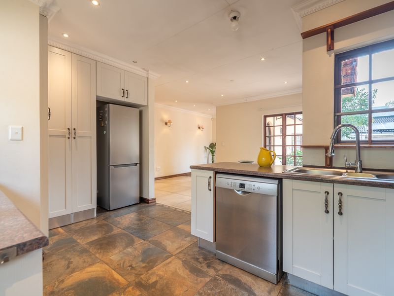 A well-maintained kitchen featuring light-toned cabinetry, dark laminate countertops, tiled flooring, and integrated dishwasher, flowing into an adjacent living area.