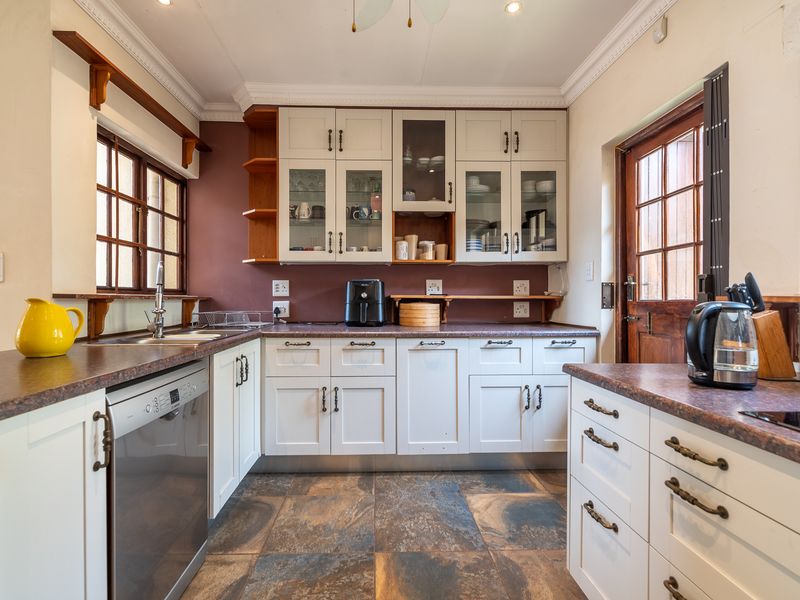 A well-maintained kitchen featuring classic white cabinetry, dark laminate countertops, tiled flooring, and direct access to the exterior via a timber-framed door.
