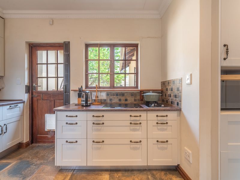 A functional kitchen featuring white cabinetry, dark laminate countertops, a tiled splashback, and direct access to the exterior via a timber-framed glass door.