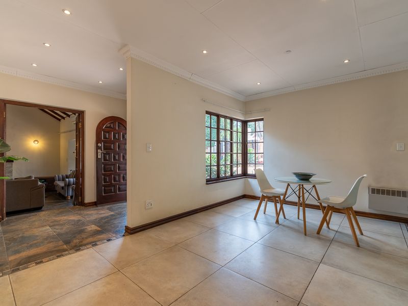 A bright living area featuring large timber-framed windows, tiled flooring, recessed downlighting, and a solid timber front door leading to an adjacent room.