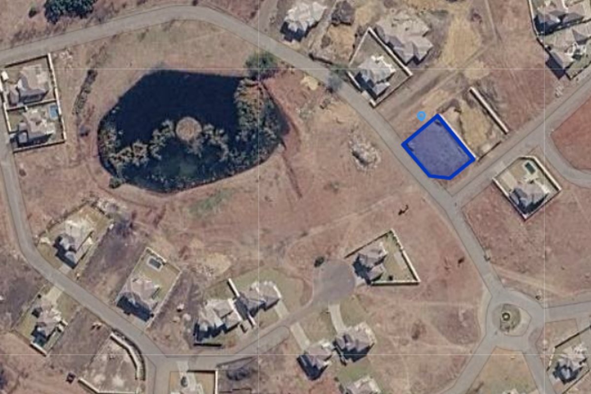 An aerial view of a vacant residential plot within a developed estate, highlighting the property boundaries and surrounding neighborhood layout.