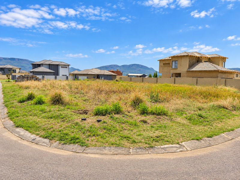 A vacant residential plot situated on a corner lot, featuring established boundary walls and mountain views in a developing neighborhood.