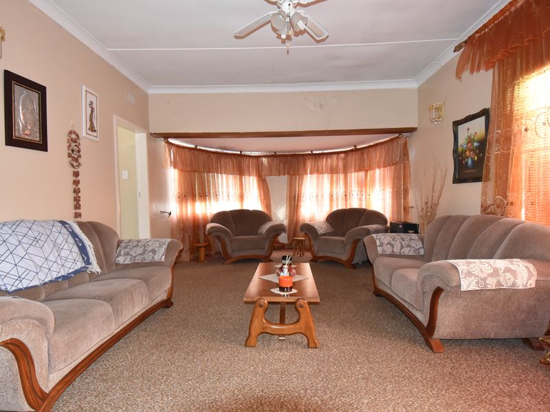 A dated living room featuring carpet flooring, a ceiling fan, and cove cornicing, currently showing signs of ceiling water damage and peeling paint.