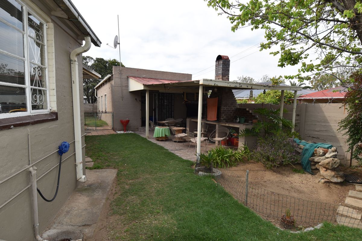 Rear garden area featuring a covered patio with a built-in brick braai, paved flooring, and a small lawn.