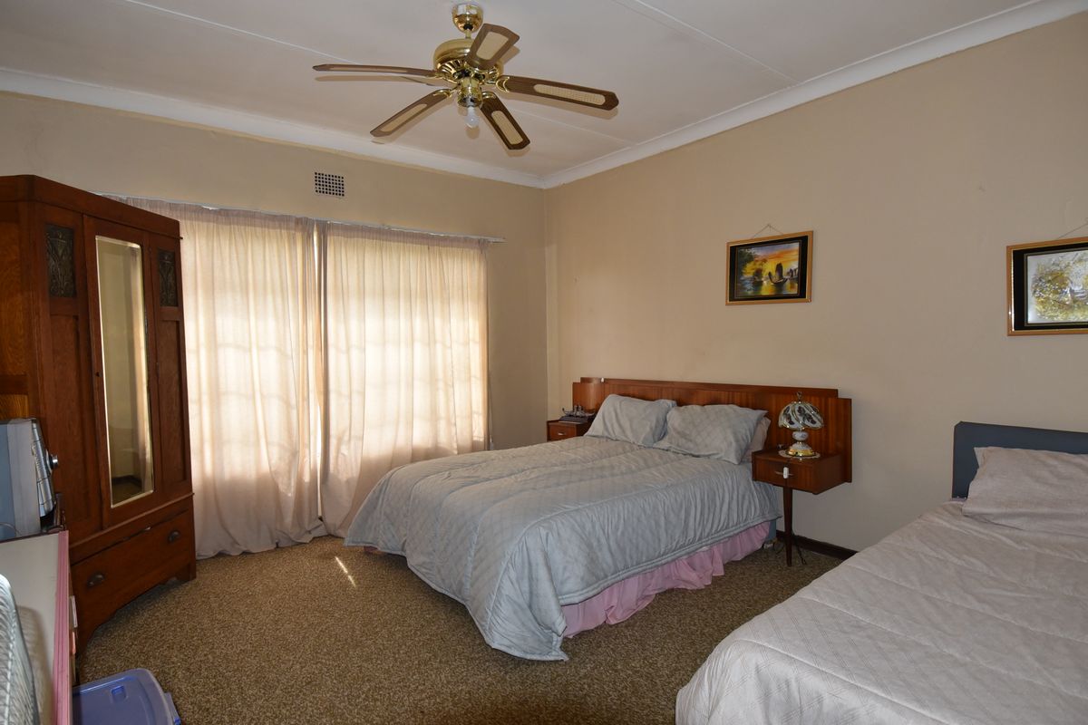 A spacious bedroom featuring a ceiling fan, built-in headboard with integrated bedside tables, and carpeted flooring.